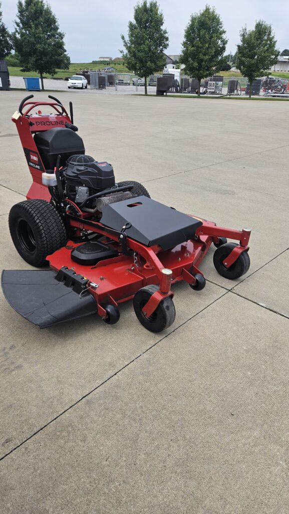 Red ProLine riding lawn mower on a concrete surface with a black engine cover and deck, large rear wheels, and a padded seat.