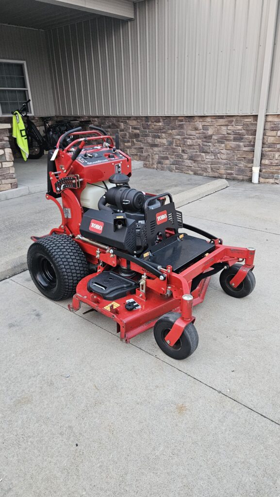Red Toro riding lawn mower with large rear tires and control levers, parked on concrete outside a building.